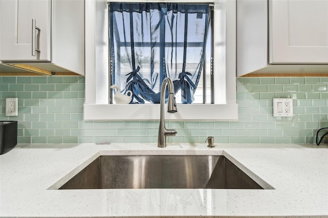 room details with sink, decorative backsplash, light stone countertops, and white cabinets