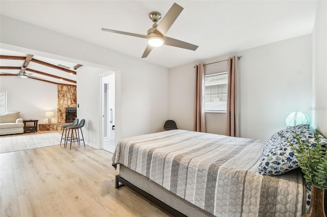 bedroom featuring vaulted ceiling with beams, ceiling fan, a fireplace, and light wood-type flooring