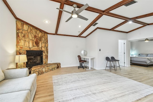 living room featuring a stone fireplace, vaulted ceiling with beams, hardwood / wood-style floors, and ceiling fan