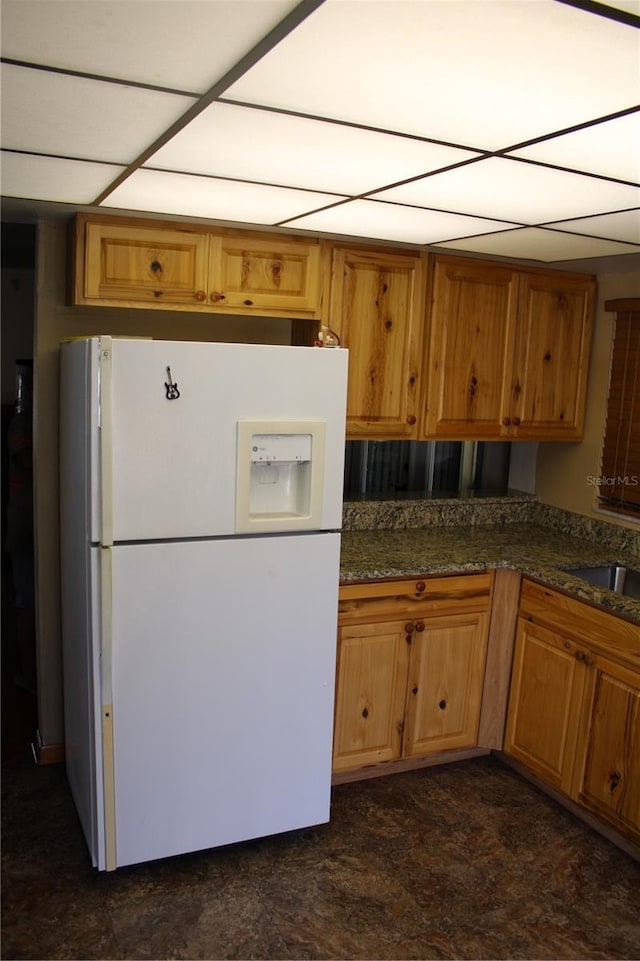 kitchen featuring white refrigerator with ice dispenser, sink, and dark stone countertops