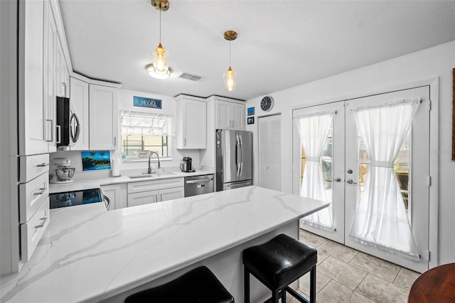 kitchen featuring sink, white cabinetry, hanging light fixtures, stainless steel appliances, and light stone countertops