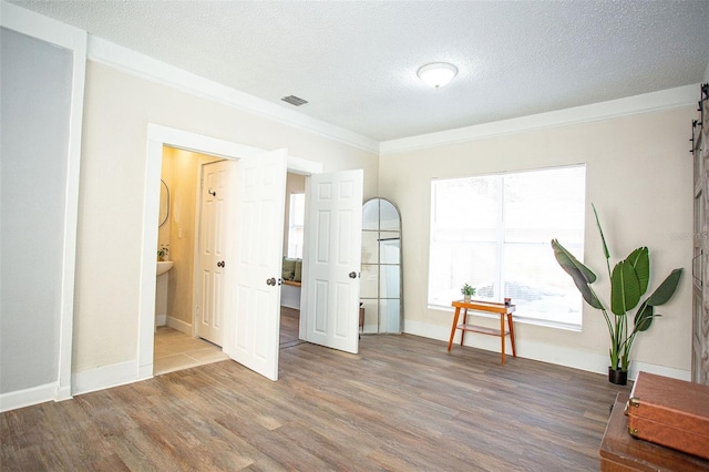 interior space with wood-type flooring, ornamental molding, and a textured ceiling