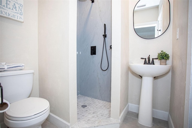 bathroom with tile patterned flooring, tiled shower, sink, and toilet