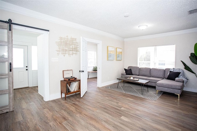 living room featuring wood-type flooring, ornamental molding, a barn door, and a textured ceiling