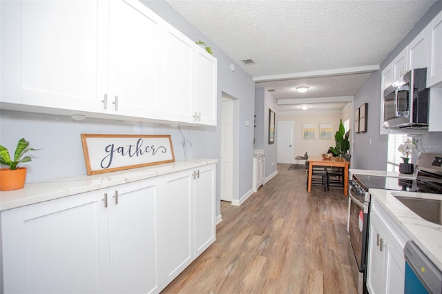 kitchen with a textured ceiling, light hardwood / wood-style flooring, appliances with stainless steel finishes, light stone countertops, and white cabinets