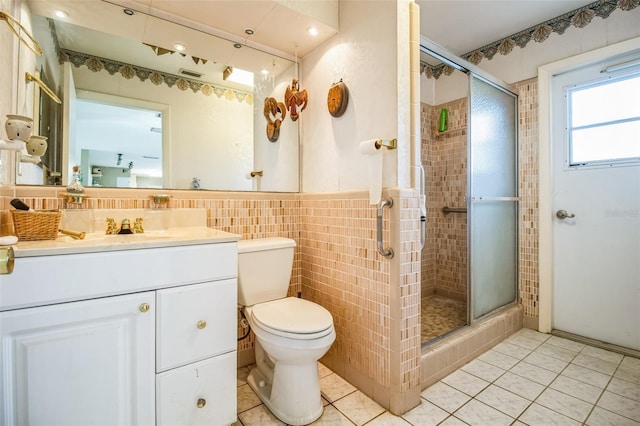 bathroom with toilet, tile walls, vanity, and a shower with shower door