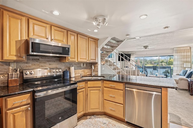 kitchen with sink, dark stone countertops, appliances with stainless steel finishes, kitchen peninsula, and decorative backsplash