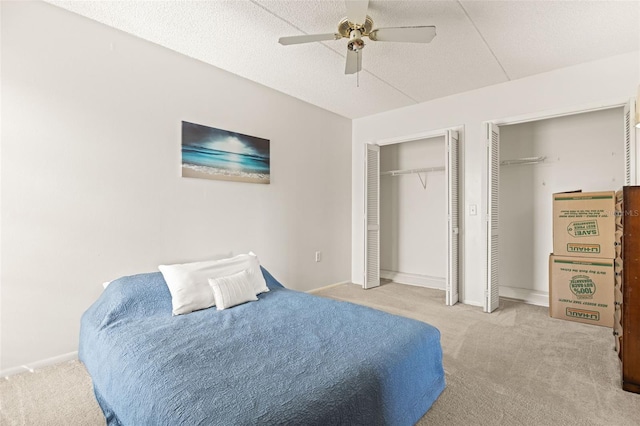 carpeted bedroom featuring two closets, a textured ceiling, and ceiling fan