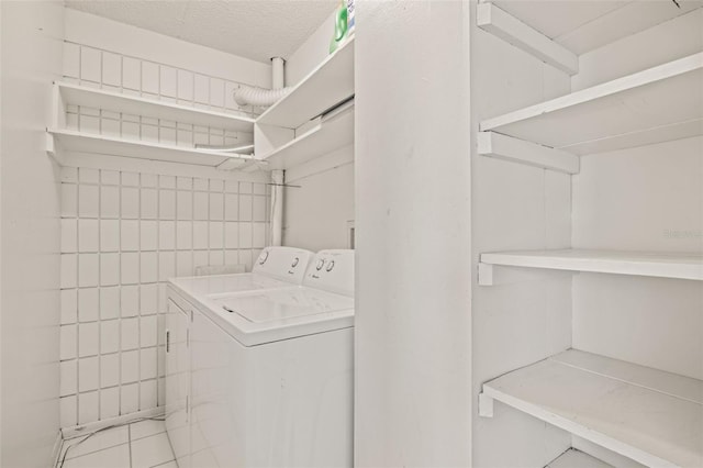 laundry area with light tile patterned floors, washer and clothes dryer, and a textured ceiling