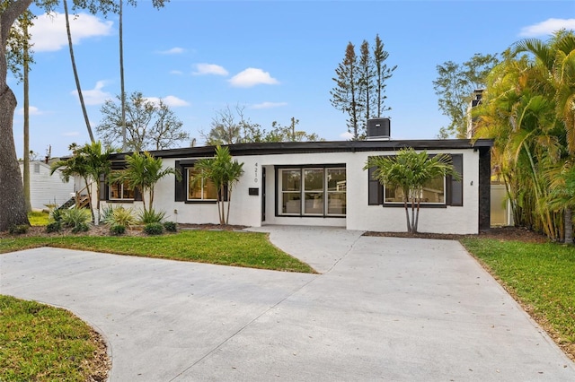 view of front facade with a front yard, central AC unit, and stucco siding