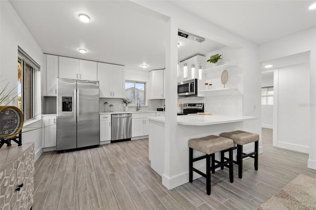 kitchen featuring light wood finished floors, open shelves, stainless steel appliances, light countertops, and white cabinetry