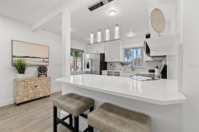 kitchen with light wood-style flooring, appliances with stainless steel finishes, a peninsula, hanging light fixtures, and a kitchen bar