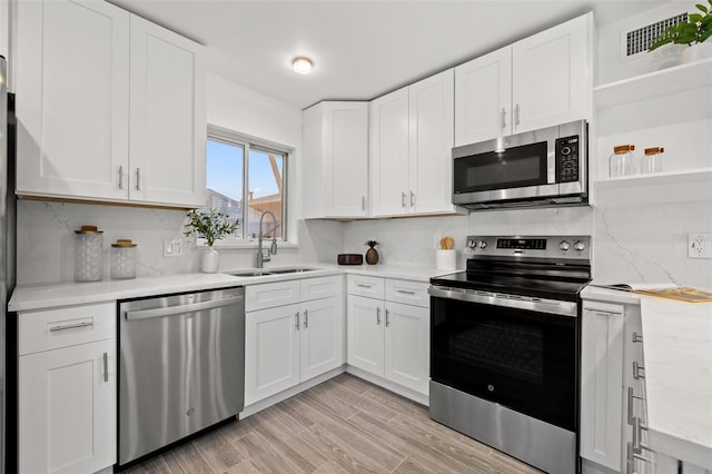 kitchen featuring stainless steel appliances, a sink, visible vents, white cabinets, and backsplash