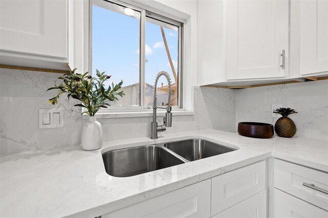 kitchen with light stone counters, white cabinetry, backsplash, and a sink