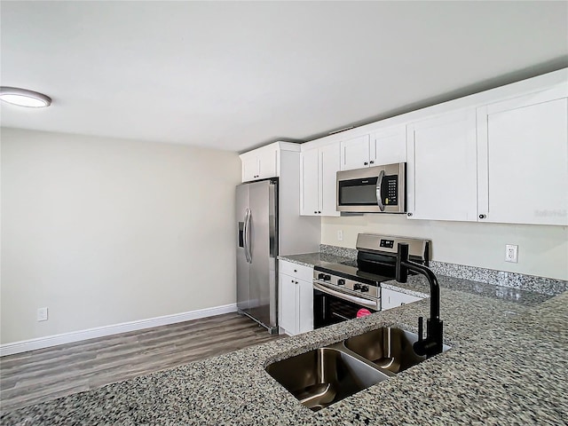 kitchen with sink, white cabinetry, dark stone counters, dark hardwood / wood-style flooring, and stainless steel appliances