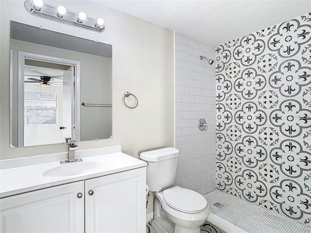 bathroom featuring ceiling fan, tiled shower, vanity, and toilet