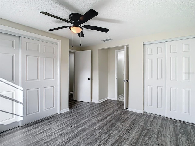 unfurnished bedroom with a textured ceiling, ceiling fan, and two closets