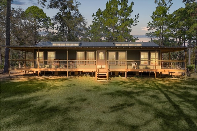 back house at dusk featuring a wooden deck and a yard