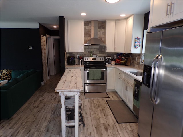 kitchen with wall chimney exhaust hood, tasteful backsplash, appliances with stainless steel finishes, light hardwood / wood-style floors, and white cabinets