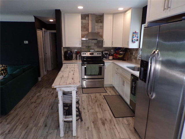 kitchen featuring stainless steel appliances, tasteful backsplash, wall chimney range hood, and white cabinets