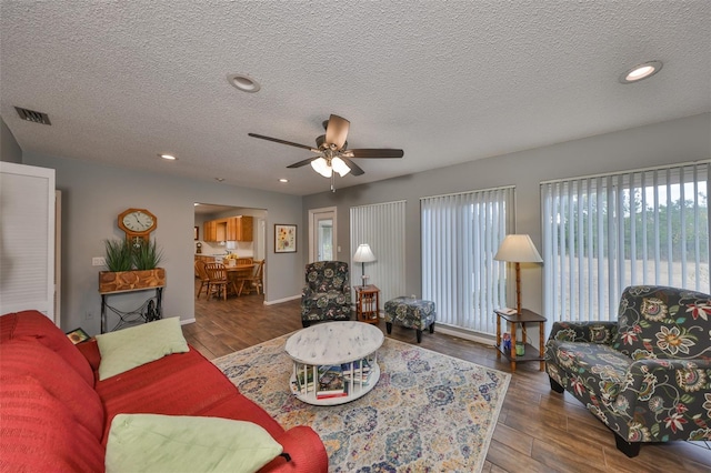 living room featuring dark hardwood / wood-style flooring, ceiling fan, and a textured ceiling