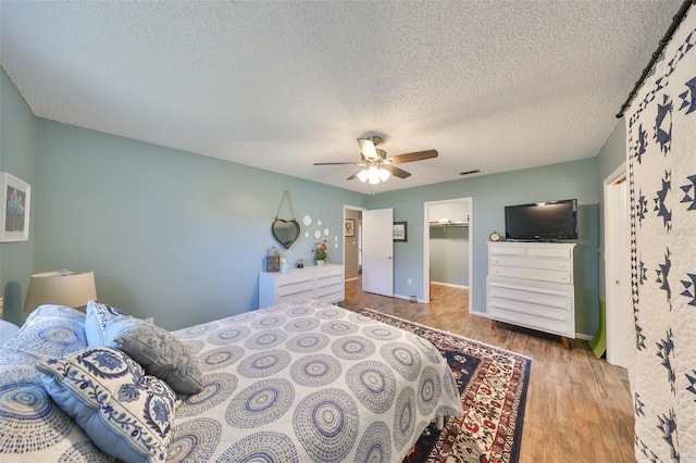 bedroom featuring a walk in closet, light hardwood / wood-style floors, ceiling fan, a textured ceiling, and a closet