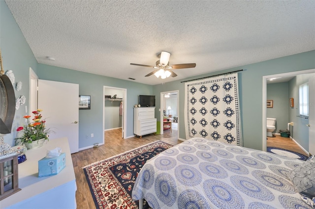 bedroom featuring ensuite bathroom, a walk in closet, wood-type flooring, a closet, and ceiling fan