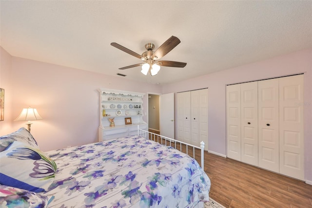 bedroom featuring hardwood / wood-style floors, two closets, a textured ceiling, and ceiling fan