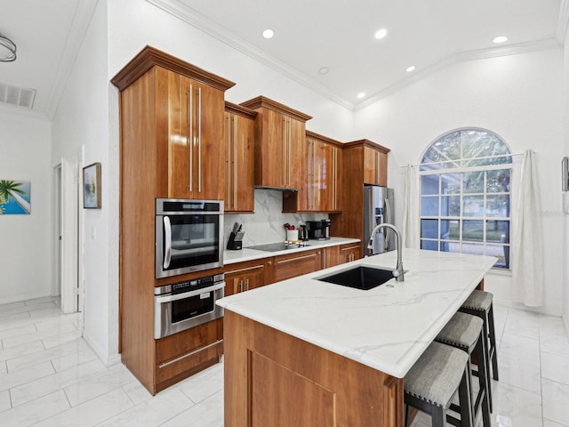 kitchen with a kitchen bar, sink, a center island with sink, appliances with stainless steel finishes, and decorative backsplash