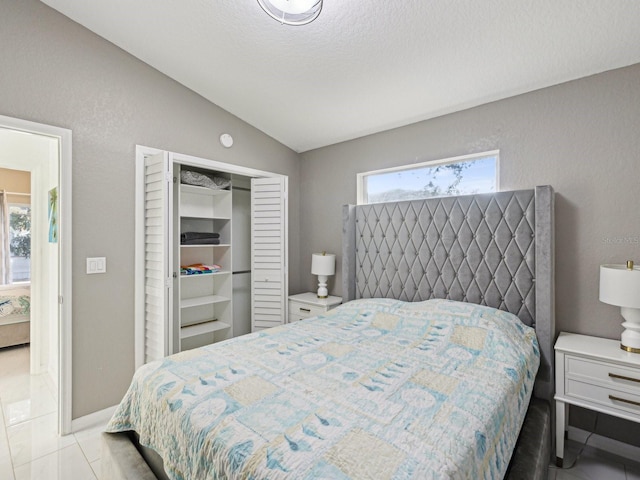 tiled bedroom with vaulted ceiling, a closet, and a textured ceiling