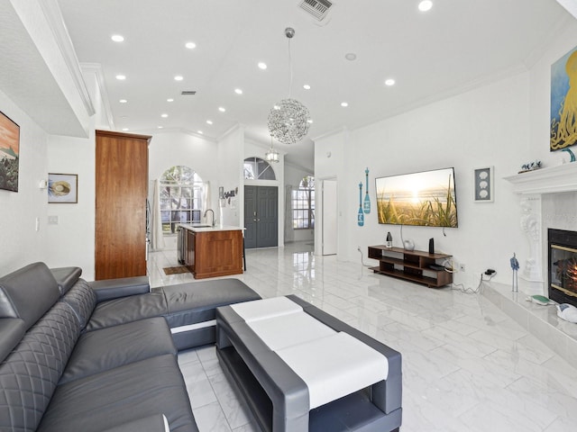 living room featuring lofted ceiling, sink, a chandelier, ornamental molding, and a premium fireplace