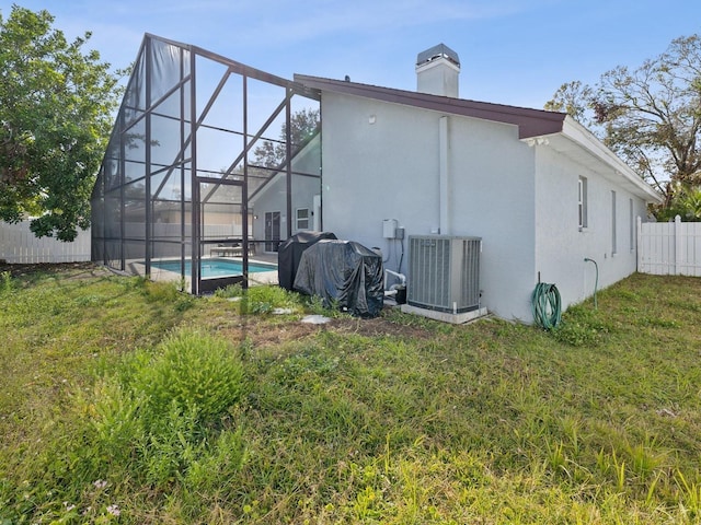 rear view of property featuring a fenced in pool, a yard, central AC unit, and glass enclosure