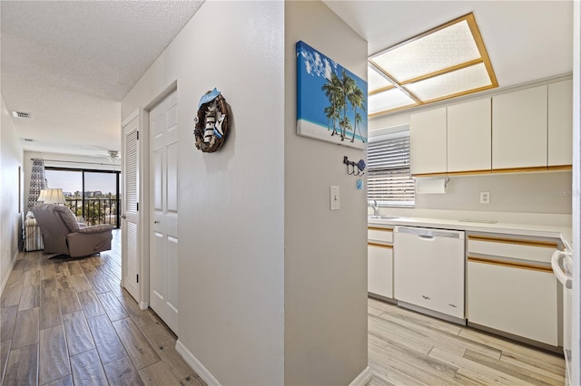 kitchen with white cabinetry, sink, white dishwasher, light hardwood / wood-style floors, and a textured ceiling