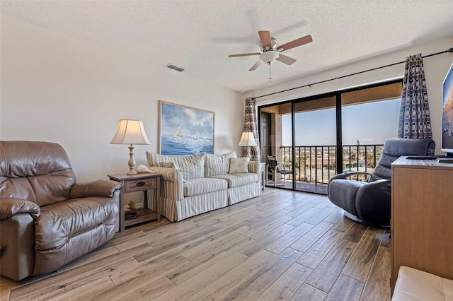 living room featuring ceiling fan, a textured ceiling, and light hardwood / wood-style floors