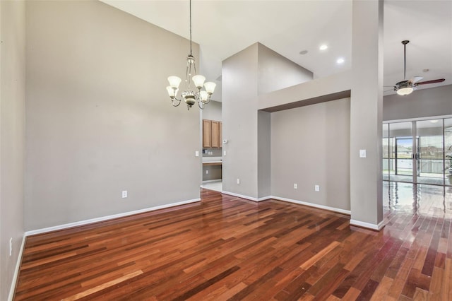 unfurnished living room featuring a towering ceiling, ceiling fan with notable chandelier, and dark hardwood / wood-style floors