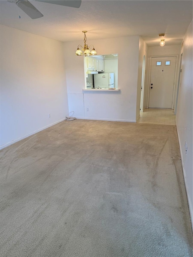 spare room featuring light colored carpet, baseboards, ceiling fan, a chandelier, and arched walkways
