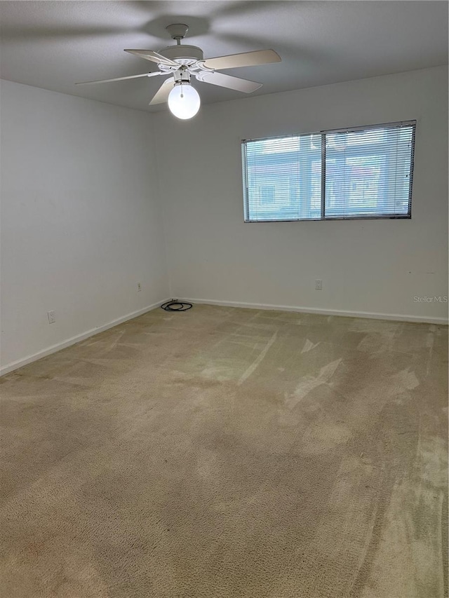 carpeted empty room featuring a ceiling fan and baseboards