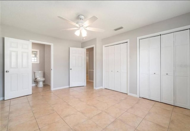 unfurnished bedroom with ensuite bathroom, two closets, ceiling fan, and light tile patterned floors