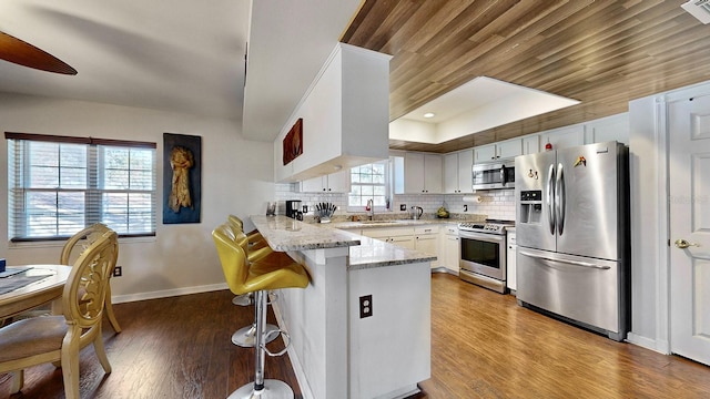 kitchen featuring stainless steel appliances, kitchen peninsula, a breakfast bar area, and white cabinets