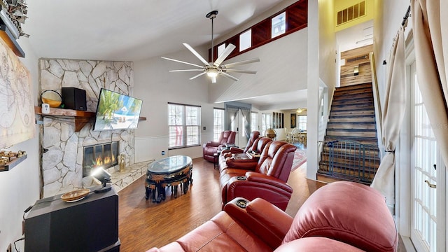 living room featuring wood-type flooring, a stone fireplace, high vaulted ceiling, and ceiling fan