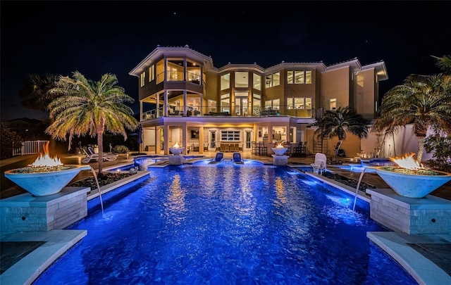 pool at twilight with pool water feature, an outdoor fire pit, and a patio