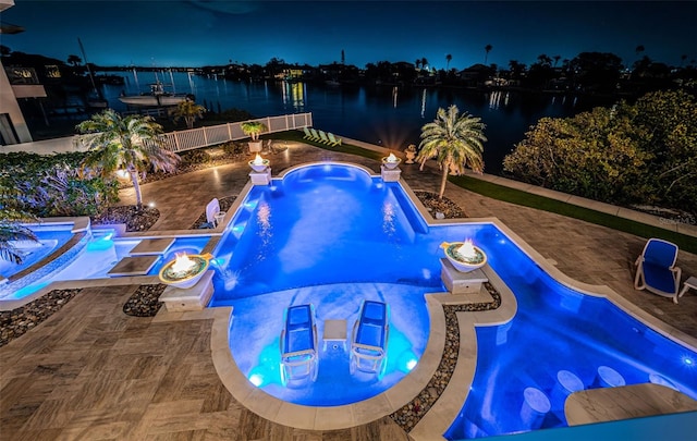 pool at night featuring an in ground hot tub, a water view, pool water feature, and a patio area