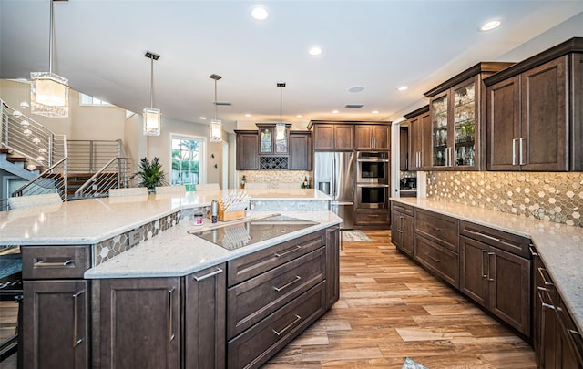 kitchen featuring pendant lighting, appliances with stainless steel finishes, dark brown cabinets, and a large island with sink