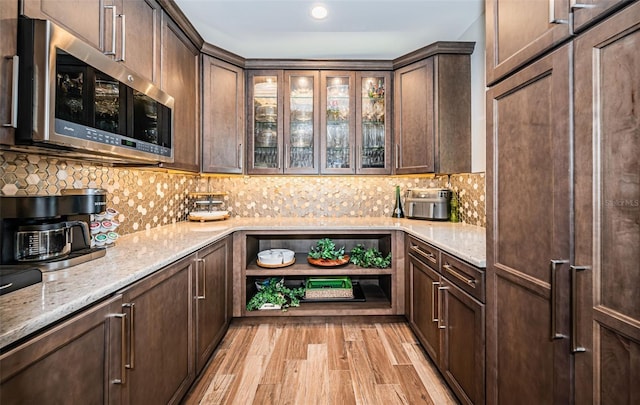 bar featuring light stone counters, dark brown cabinets, and light wood-type flooring