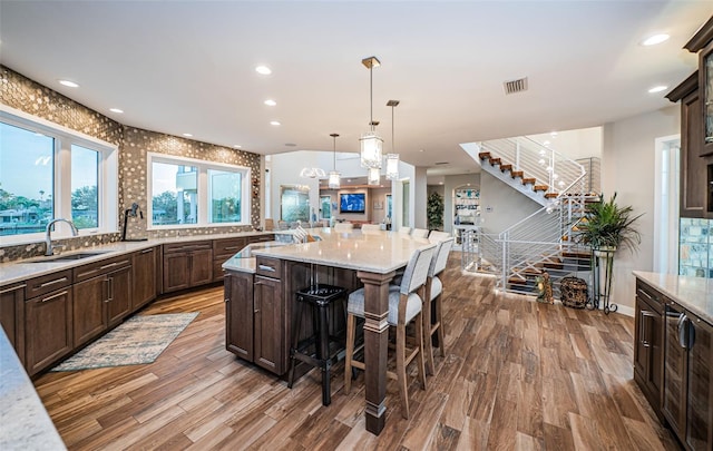 kitchen with a kitchen bar, sink, light stone counters, a kitchen island, and pendant lighting