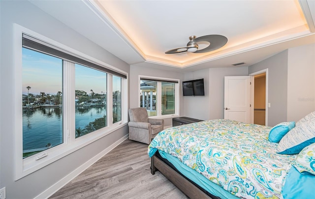 bedroom featuring ceiling fan, light wood-type flooring, and a tray ceiling