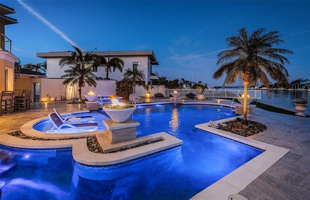 pool at dusk with pool water feature, an outdoor fire pit, an in ground hot tub, and a patio