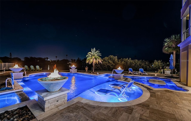 pool at night featuring pool water feature, an in ground hot tub, and a patio