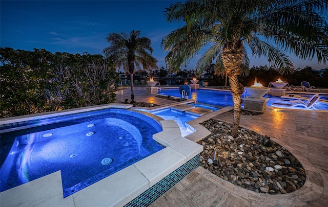 pool at dusk with an in ground hot tub, pool water feature, and a patio area