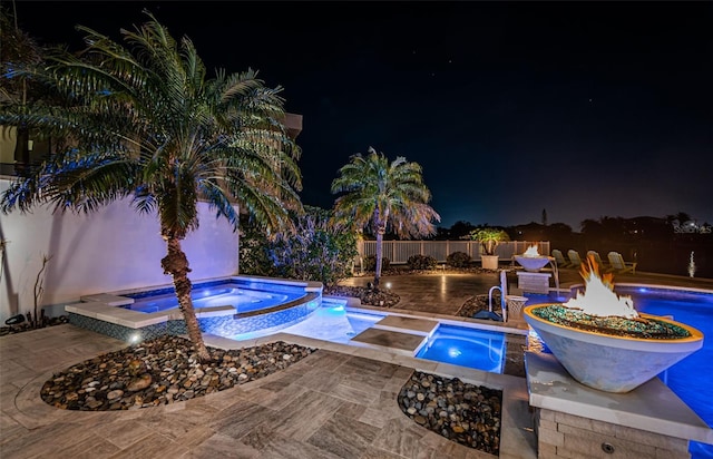 pool at night with a patio and an in ground hot tub